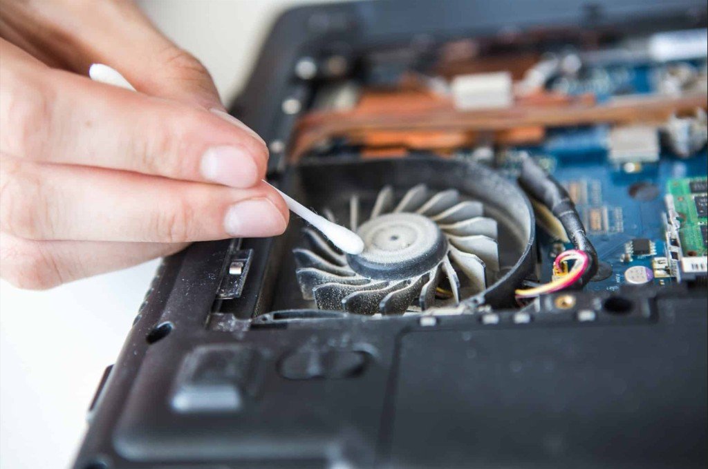 Technician cleaning dust from a laptop cooling fan during overheating repair